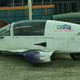 Just a land-plane in front of an Opel GT and next to a covered wagon is all